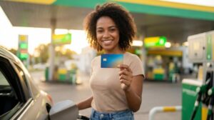 Pessoa brasileira sorrindo segurando um cartão perto da bomba em posto com cores da Petrobras